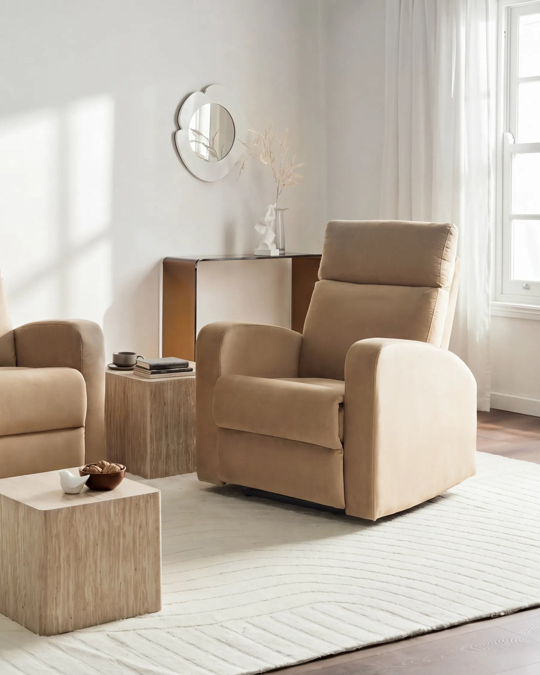 A beige upholstered recliner chair shown in a bright, modern living room with matching furniture, a side table, rug, and window.