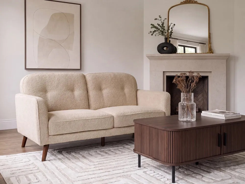 A cream-colored tufted loveseat sofa in a modern living room setting, positioned next to a dark wood coffee table and in front of a fireplace.