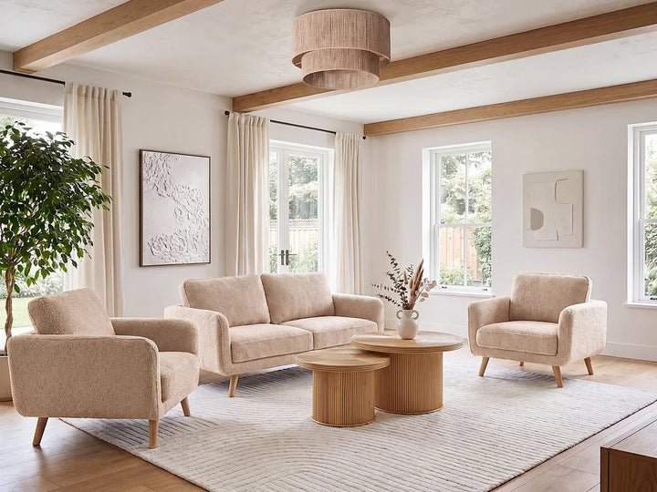 A styled living room featuring a beige upholstered three-seat sofa, two matching armchairs, two round wooden coffee tables, a large textured light rug, and a natural wood ceiling with exposed beams.