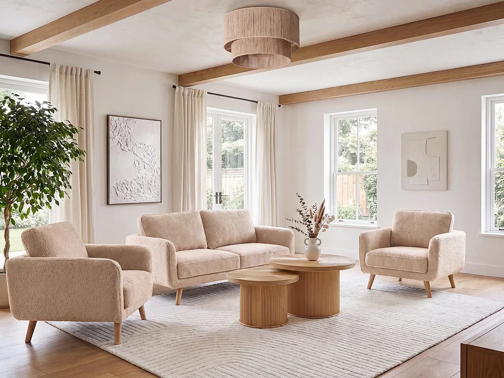 A styled living room featuring a beige upholstered three-seat sofa, two matching armchairs, two round wooden coffee tables, a large textured light rug, and a natural wood ceiling with exposed beams.