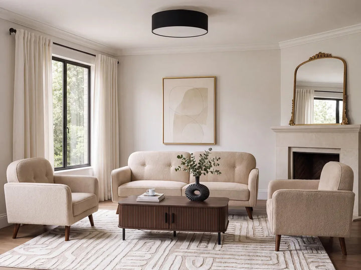A styled living room featuring a beige tufted sofa, two matching armchairs, a dark wood coffee table, and a patterned rug, set against cream walls with a fireplace, window with curtains, and a black drum ceiling light.