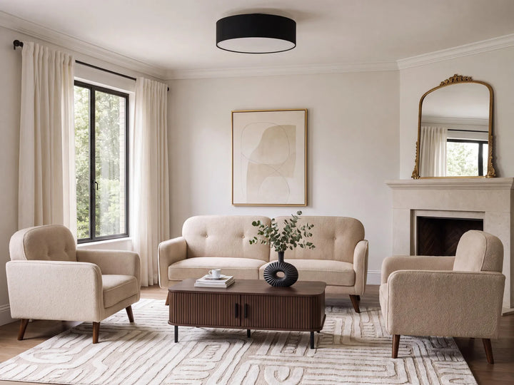 A styled living room featuring a beige tufted sofa, two matching armchairs, a dark wood coffee table, and a patterned rug, set against cream walls with a fireplace, window with curtains, and a black drum ceiling light.