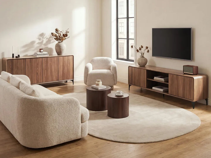 A styled living room featuring a cream bouclé sofa, matching armchair, round coffee tables, a sideboard, a TV console, and a large oval area rug on a light wood floor.