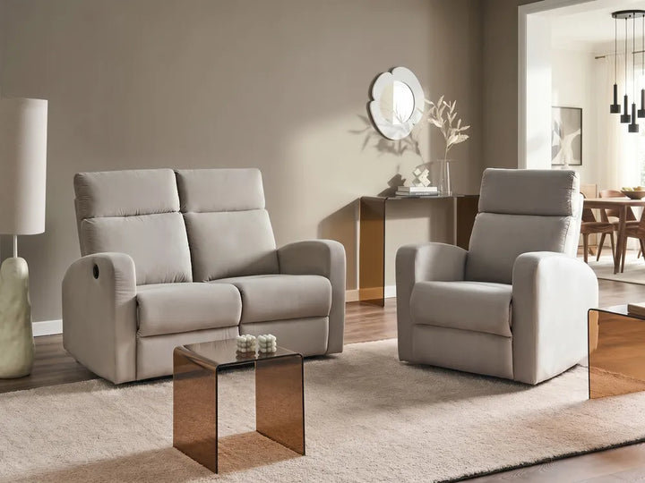 A light beige upholstered loveseat and matching recliner chair arranged in a modern living room with a glass-top side table, rug, lamp, and wall decor.