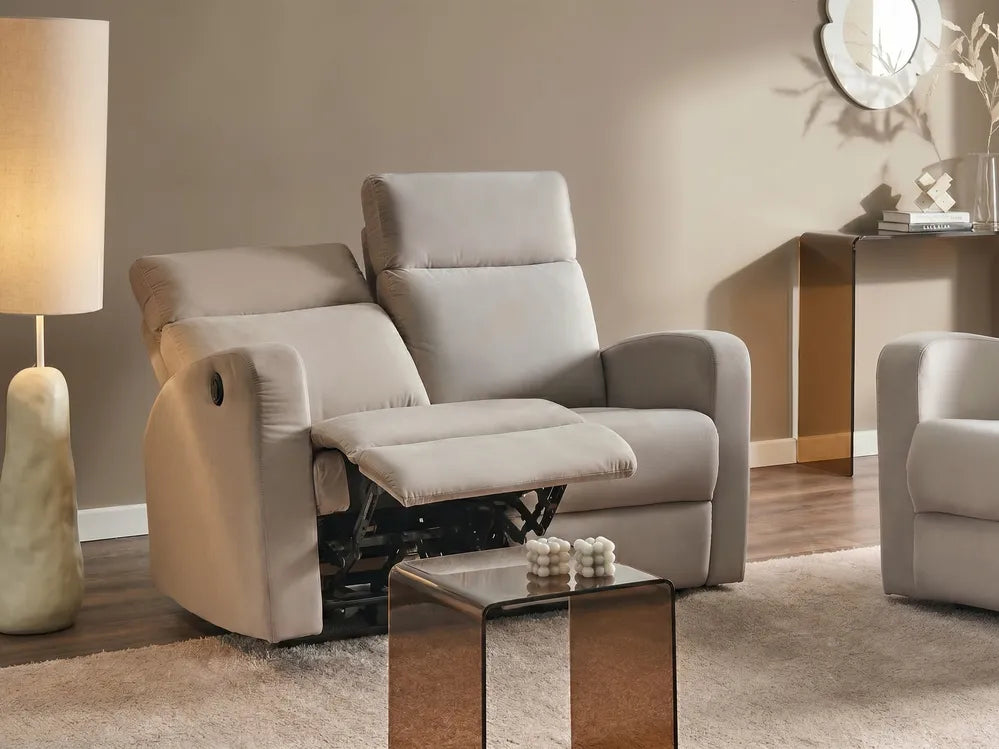A light beige recliner chair with the footrest extended, shown in a styled living room setting with a floor lamp, side table, and another matching chair partially visible.