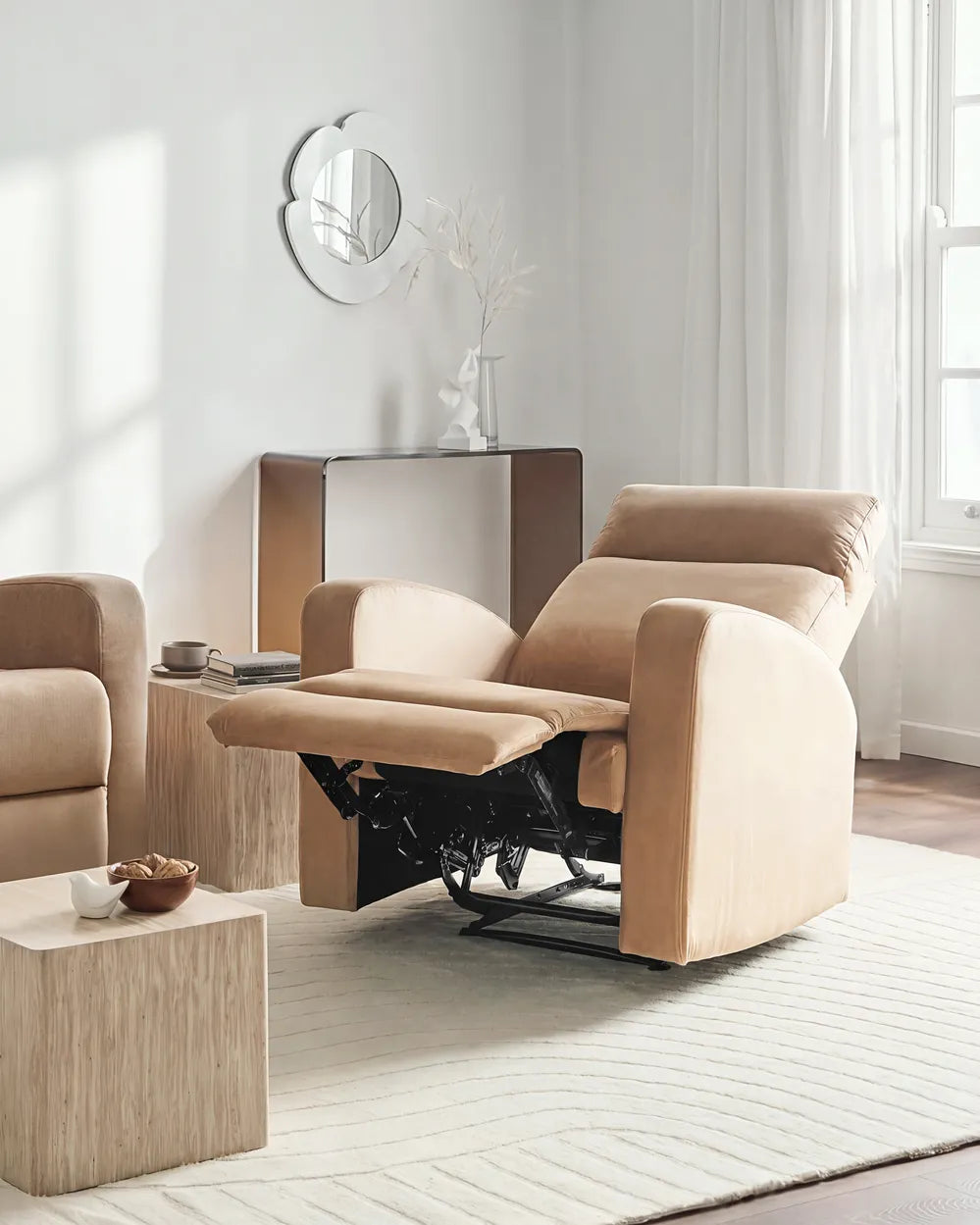 A beige upholstered recliner chair with the footrest extended, shown in a bright, modern living room setting with a matching armchair, side table, and neutral decor.