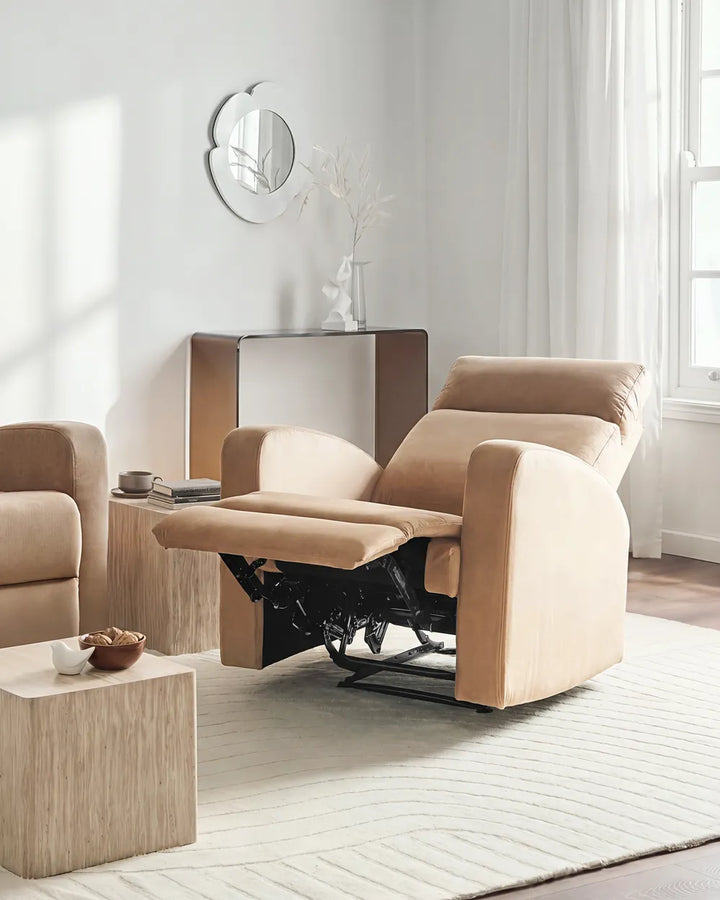 A beige upholstered recliner chair with the footrest extended, shown in a bright, modern living room setting with a matching armchair, side table, and neutral decor.