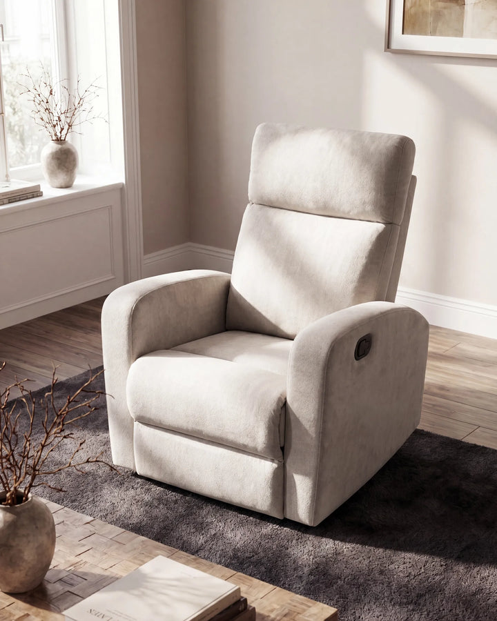 A light beige upholstered recliner chair with a high backrest, shown in a styled living room setting with a dark gray rug, wood flooring, and a window in the background.