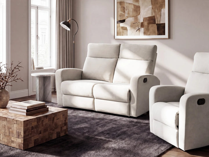 A light beige upholstered reclining loveseat sofa and matching armchair in a modern living room setting with a dark gray rug, wooden coffee table, and neutral walls.