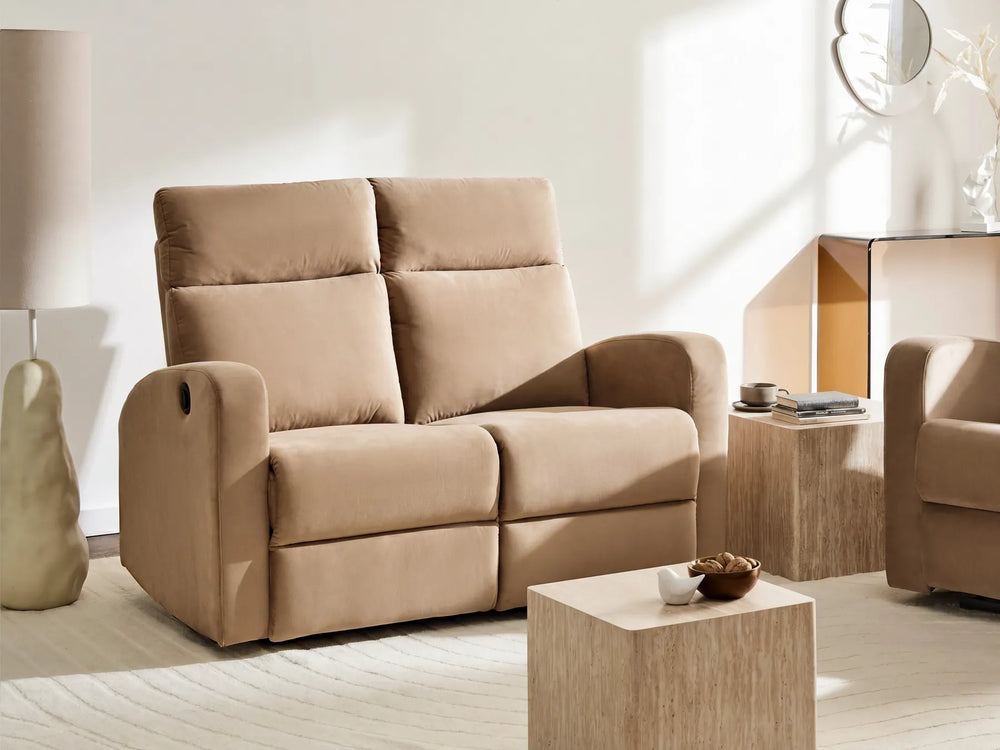 A beige upholstered reclining loveseat sofa in a modern, sunlit living room setting with matching wooden side tables and a light-colored rug.