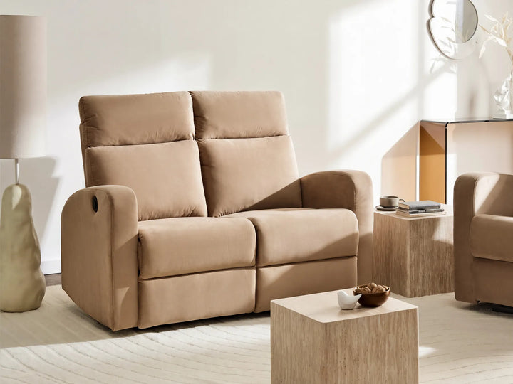 A beige upholstered reclining loveseat sofa in a modern, sunlit living room setting with matching wooden side tables and a light-colored rug.