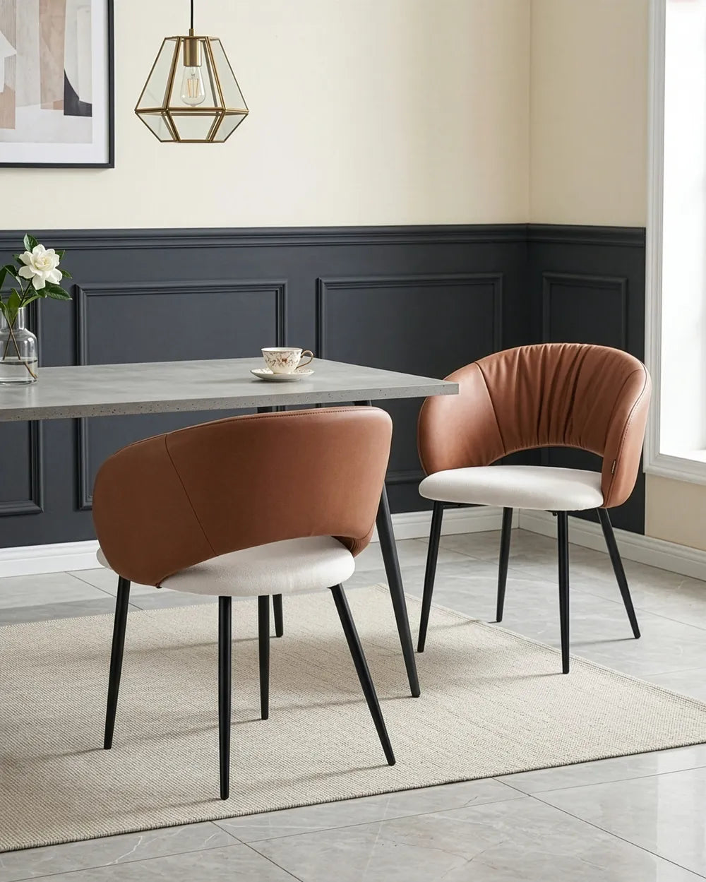 Two modern dining chairs in a styled dining room setting. One chair features a warm brown leather backrest and a white upholstered seat with black legs, while the other features a matching brown leather backrest, a cream-colored seat, and black legs.