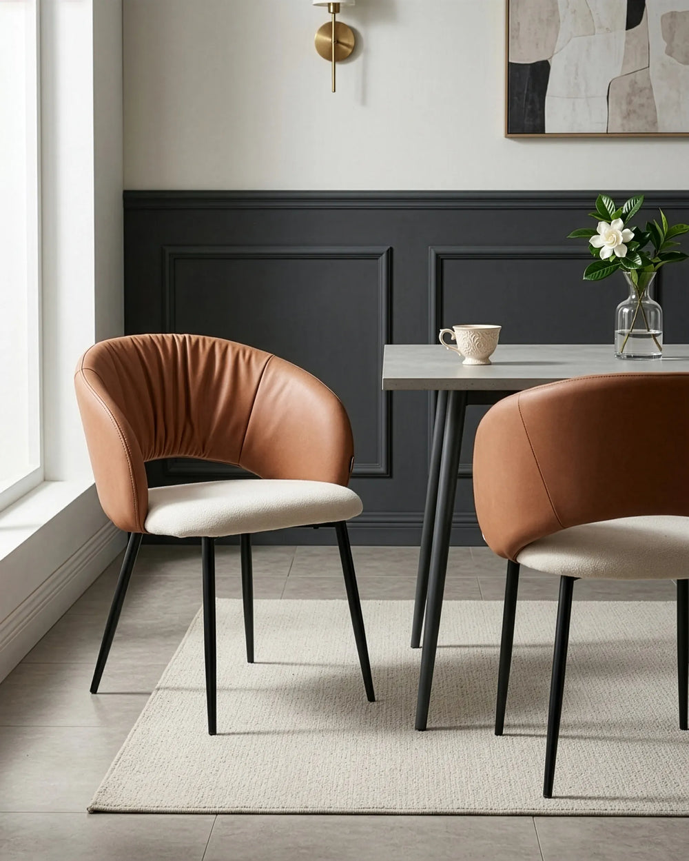 A modern dining room scene featuring two upholstered accent chairs with warm tan leather backs and cream fabric seats, positioned around a dark wood table in a styled interior.
