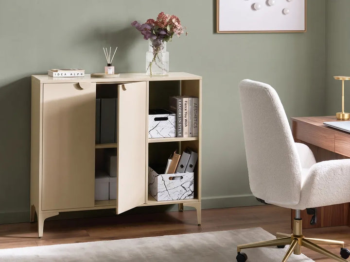 A light beige wood storage cabinet with two doors, one open, showing shelves with books and storage boxes, set in a home office next to a white textured office chair and a wooden desk.