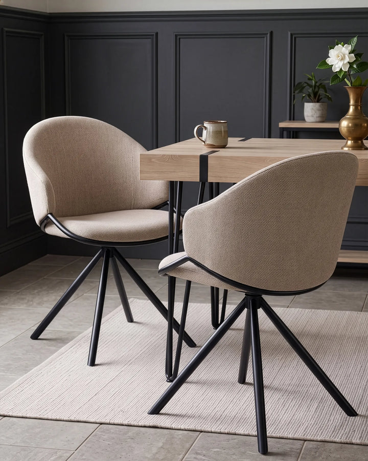 Two modern upholstered dining chairs with beige fabric and black metal legs, shown around a light wood table in a styled dining room setting.