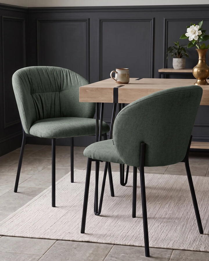 Two green upholstered dining chairs with black metal legs around a light wood table in a styled dining room setting.
