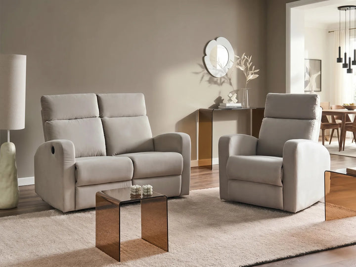 A light beige upholstered loveseat and matching recliner chair arranged in a modern living room with a glass-top side table, rug, lamp, and wall decor.