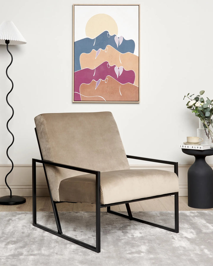 Beige armchair with black metal frame in a room with abstract art on the wall.