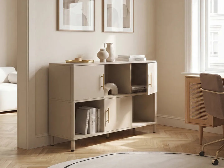 A modern two-tone beige and white storage cabinet with gold handles, styled in a warm, minimalist room with wood floors and neutral decor.