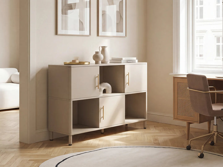 A modern beige storage cabinet with gold handles in a bright, minimalist home office setting with wood floors, a desk, and a chair.