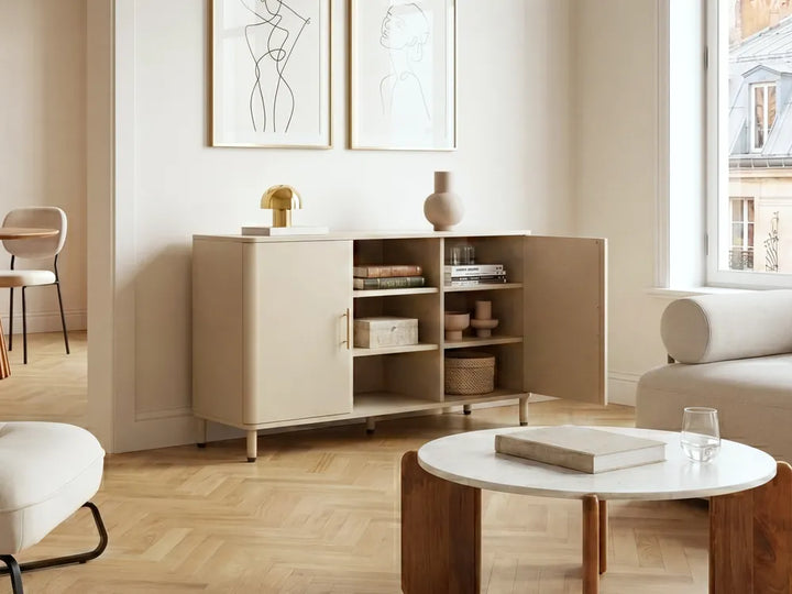 A modern beige sideboard cabinet with open doors and shelves, styled in a bright, minimalist living room with light wood floors, a white coffee table, and neutral decor.