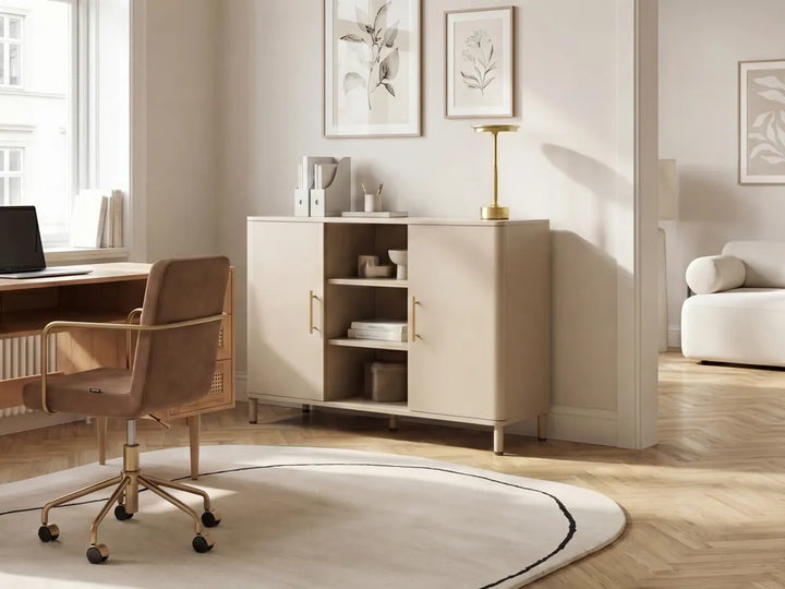 A modern beige sideboard cabinet with two doors and open shelving, styled in a bright, minimalist home office with a brown office chair, desk, and framed botanical prints on the wall.