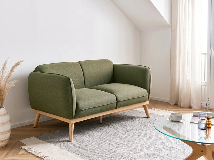 Green sofa in a modern living room with a glass coffee table and decorative items.