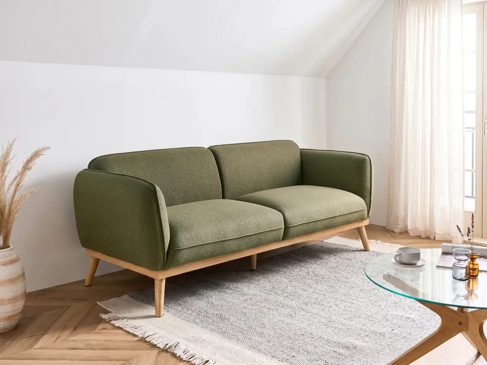 Green sofa in a modern living room with a glass coffee table and decorative items.