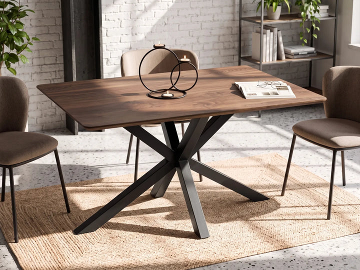 A rectangular wooden dining table with a dark metal X-shaped base, surrounded by four upholstered chairs in a bright, modern room with a white brick wall and natural light.