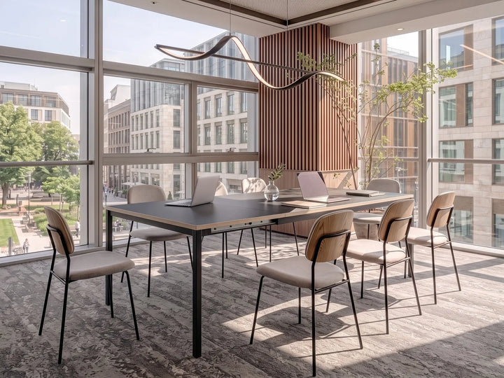 A modern conference room setup featuring a rectangular dark wood table with black metal legs, surrounded by six upholstered chairs with light beige seats and brown wood-look backs. The room is situated in a bright office with large floor-to-ceiling windows showing a city view, decorated with a wavy black pendant light and a patterned gray rug.
