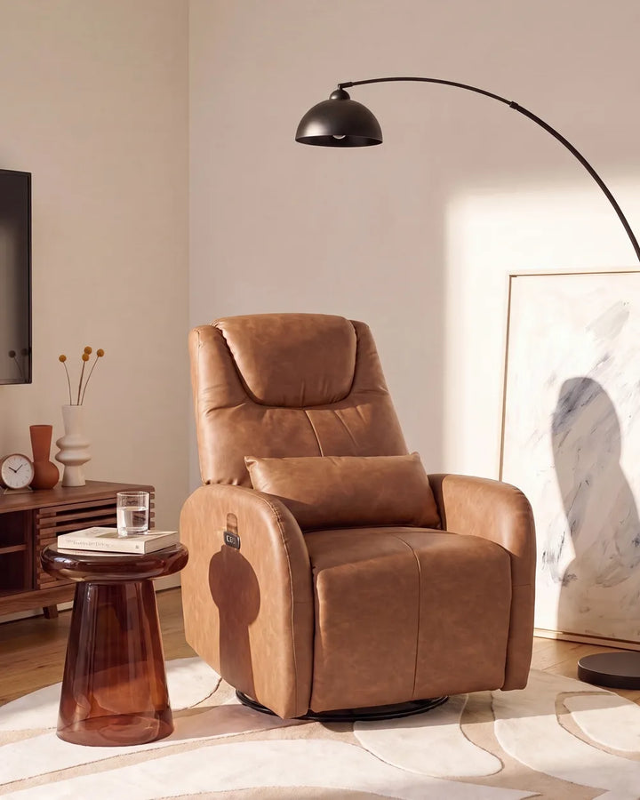 A tan leather recliner chair with a matching lumbar pillow, styled in a modern living room setting with a side table, floor lamp, and neutral-toned decor.