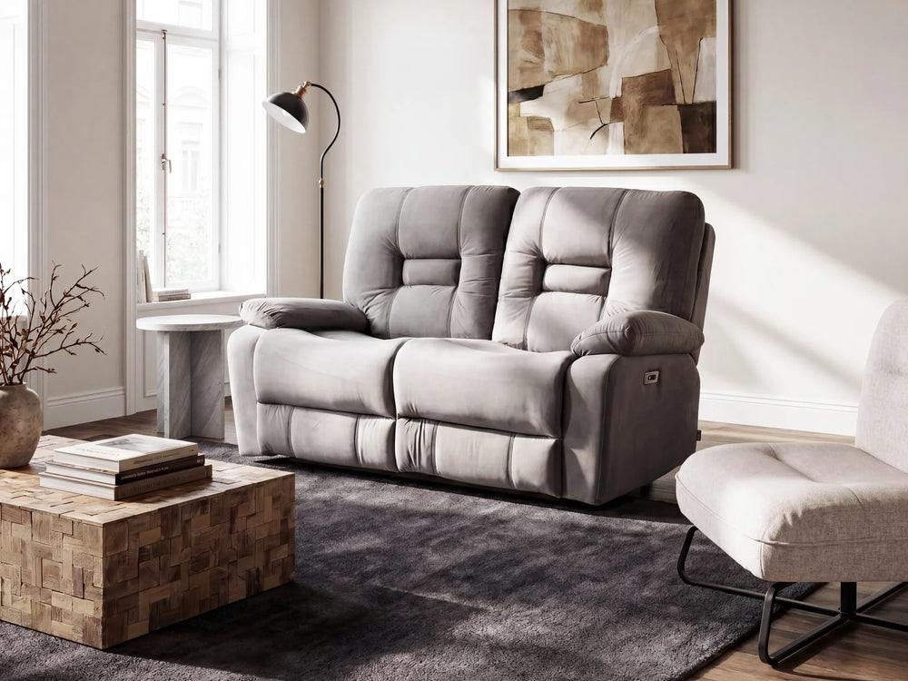 A gray two-seater reclining loveseat sofa in a modern living room setting, positioned next to a matching armchair, a wooden coffee table, and a dark gray rug.