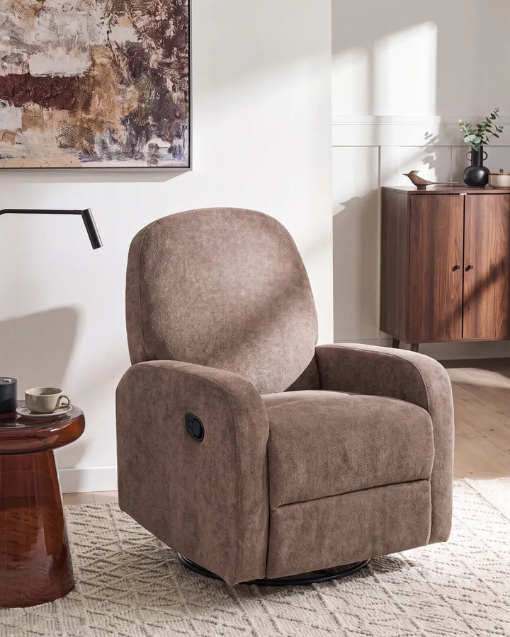 A plush upholstered recliner chair in a warm taupe-brown fabric, shown in a styled living room setting with a wooden sideboard, abstract wall art, and a patterned rug.