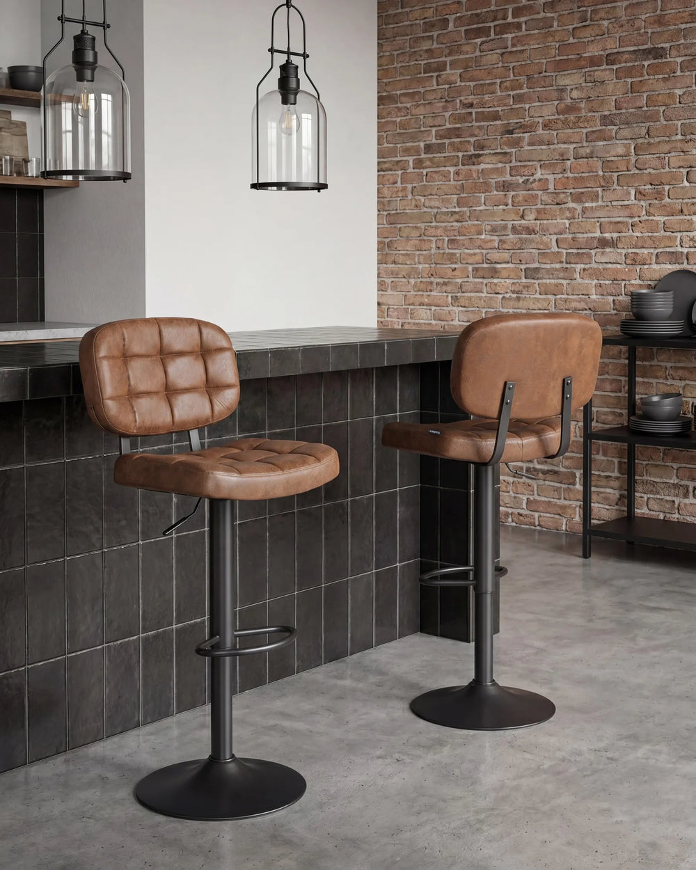 Two brown leather bar stools with black metal bases in a modern kitchen setting with a brick wall and dark tiled counter.