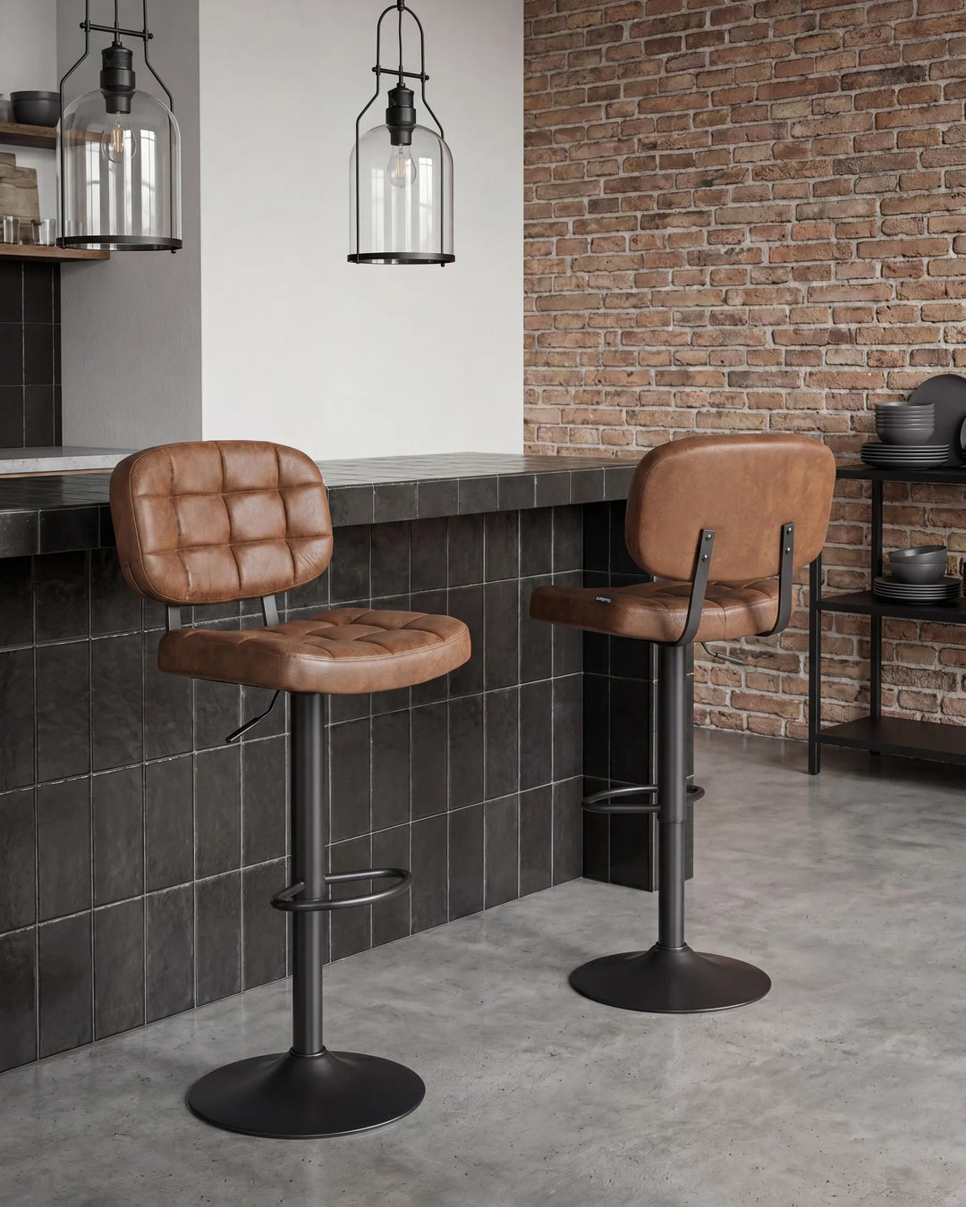 Two brown leather bar stools with black metal bases in a modern kitchen setting with a brick wall and dark tiled counter.