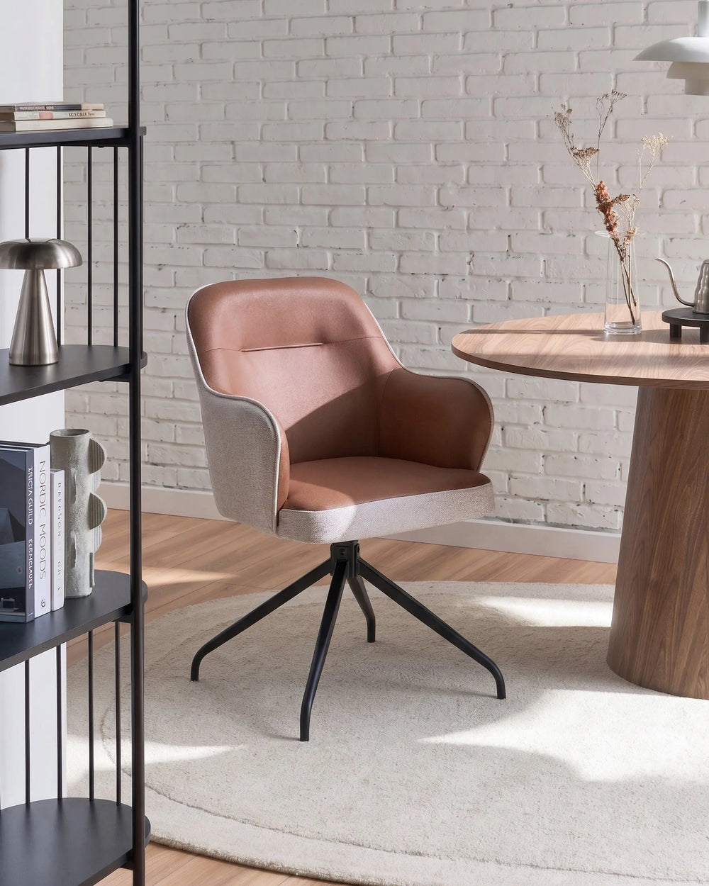 Modern chair with a wooden table and bookshelf against a brick wall.