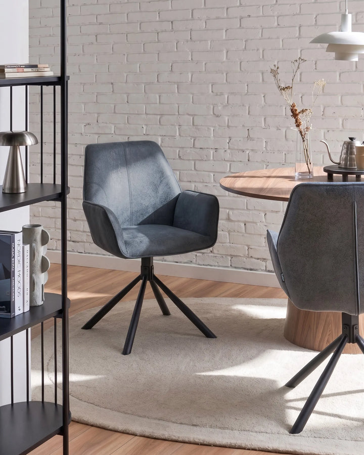 A modern gray upholstered swivel dining chair with black metal legs, shown in a styled dining room setting next to a round wooden table and another matching chair.