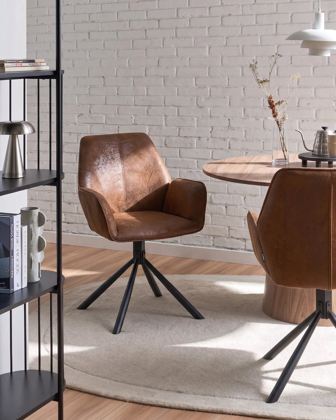 Brown leather chair in a modern interior setting with a brick wall and wooden table.