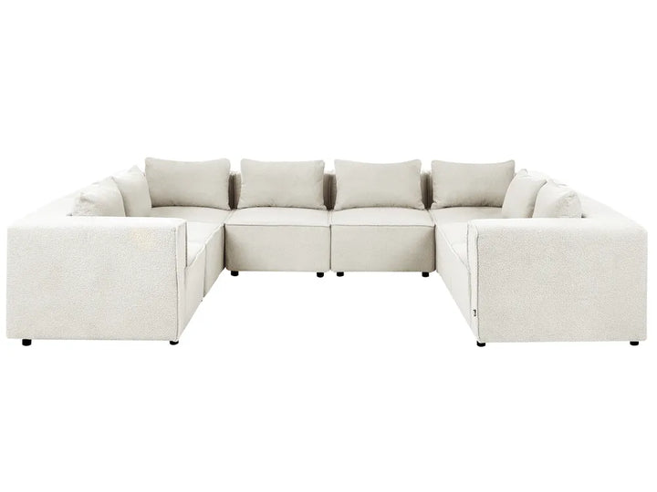A modern sectional sofa upholstered in a light beige textured fabric, featuring a left-facing chaise lounge and four matching back cushions, shown against a plain white background.