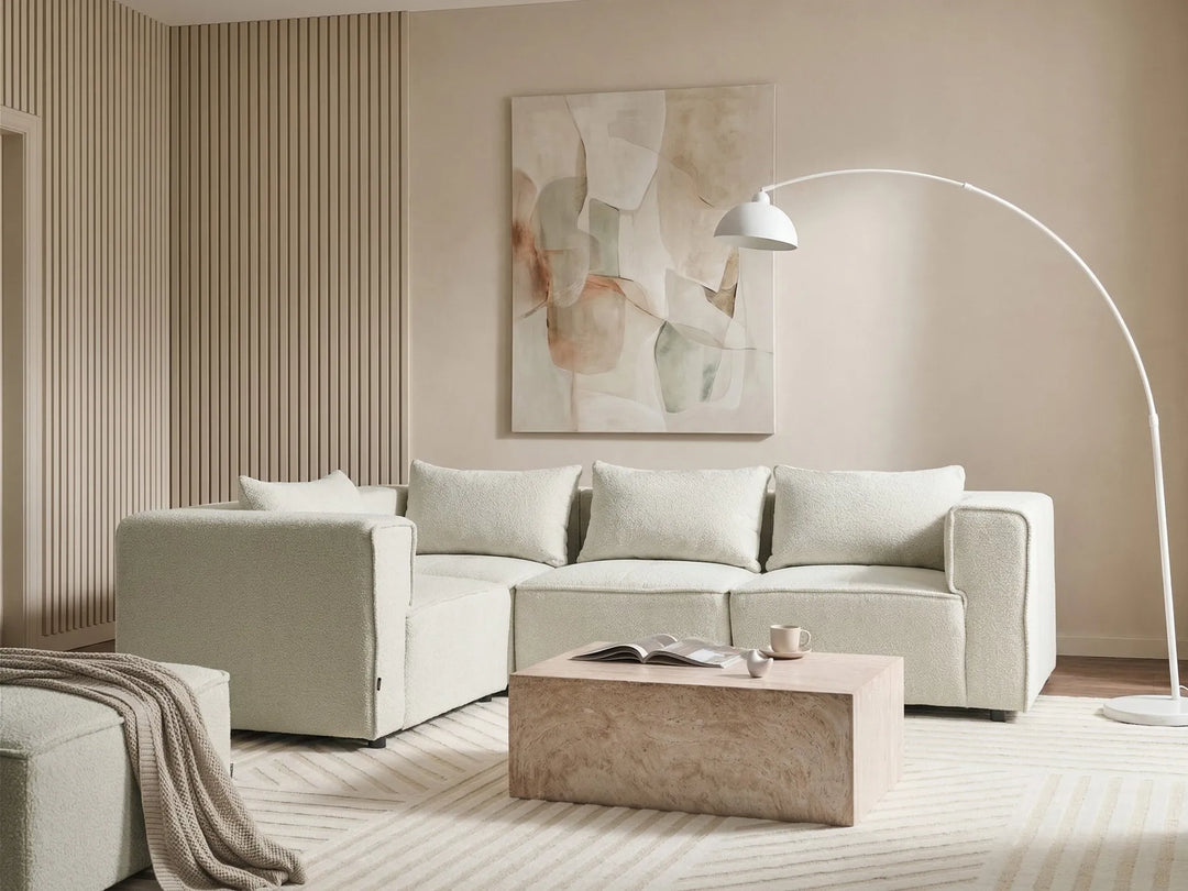 A modern living room featuring a light beige sectional sofa, a low marble coffee table, a white arched floor lamp, and a large abstract painting on the wall.