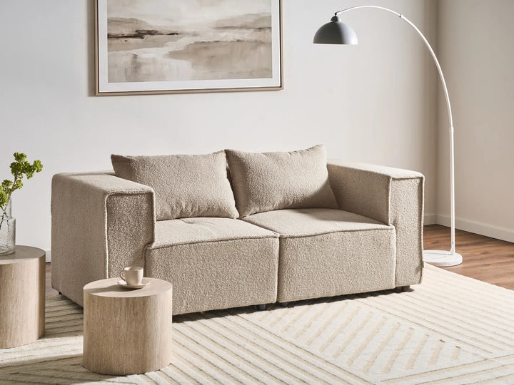 Beige sofa in a living room with a lamp, side table, and artwork on the wall.