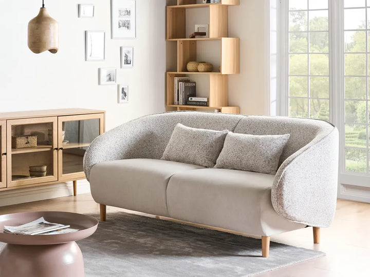 Beige sofa in a living room with wooden shelves and a window in the background