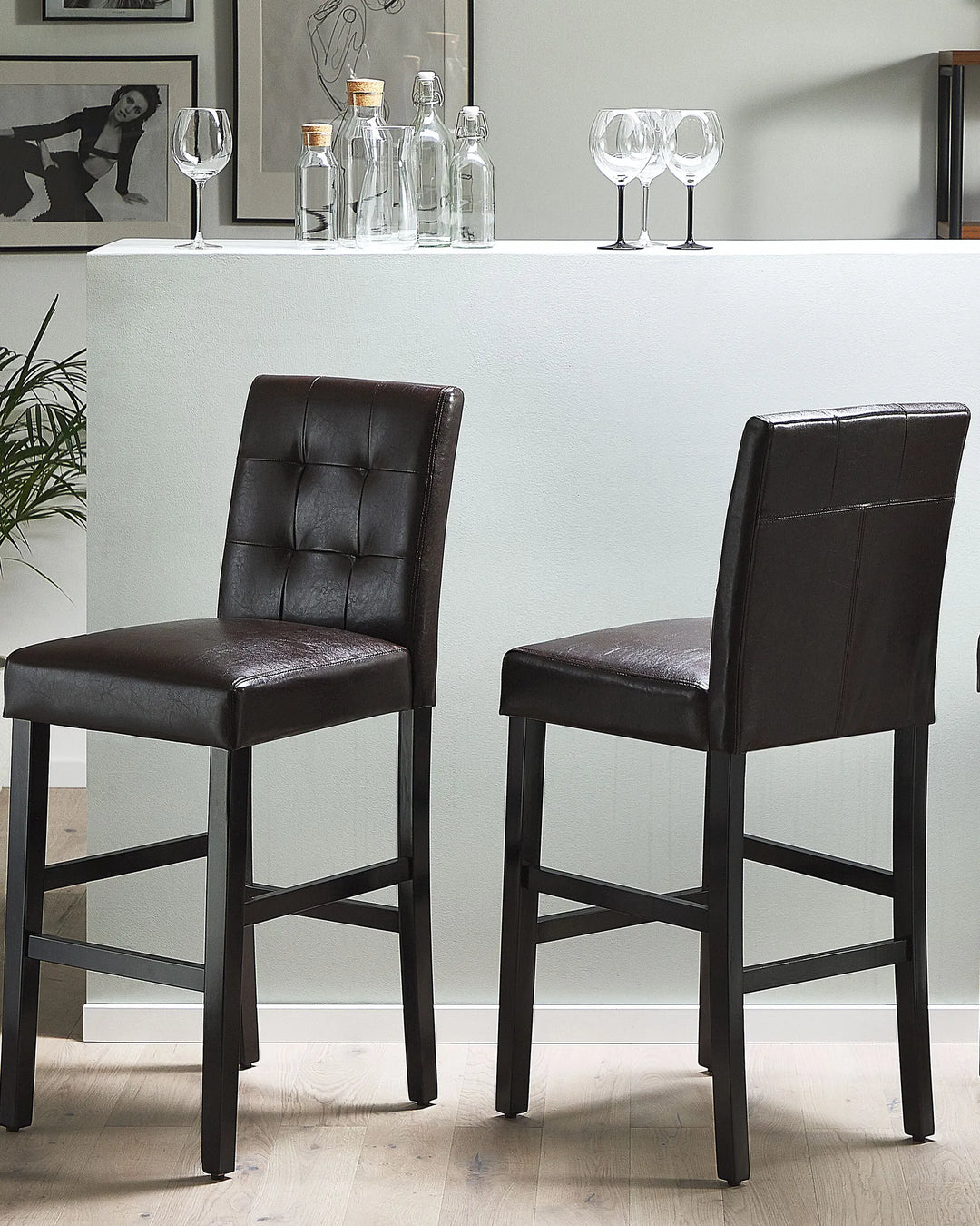 Two brown bar stools in front of a white counter with bottles and glasses.