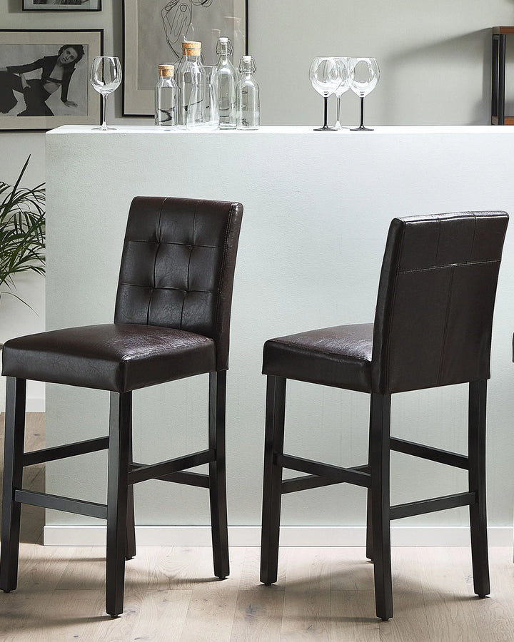Two brown bar stools in front of a white counter with bottles and glasses.