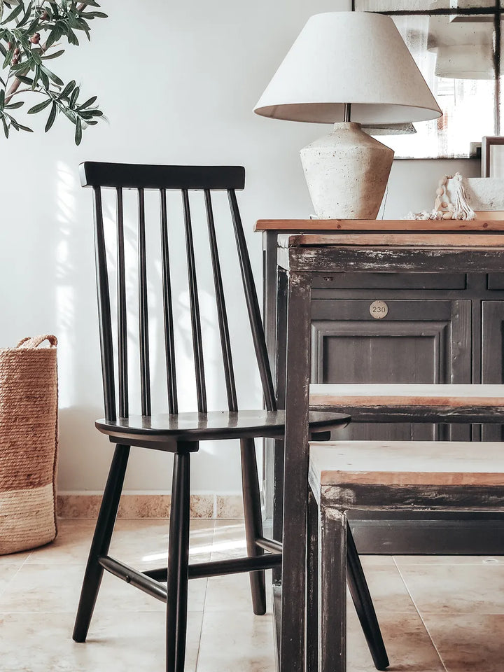 A black wooden spindle-back chair positioned next to a dark rustic table with a light wood top in a bright, modern interior setting.