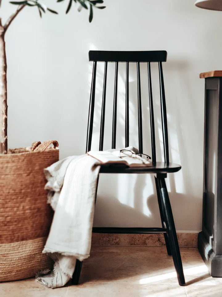 A black wooden spindle-back chair in a bright, sunlit room, styled with a white throw blanket and an open book on its seat.