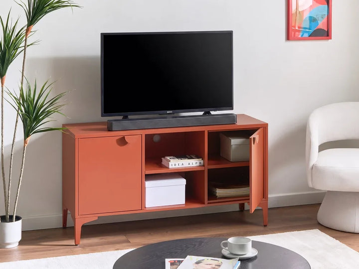 A mid-century modern orange TV stand cabinet with open shelves and a door, styled in a living room with a television, potted plant, and white armchair.