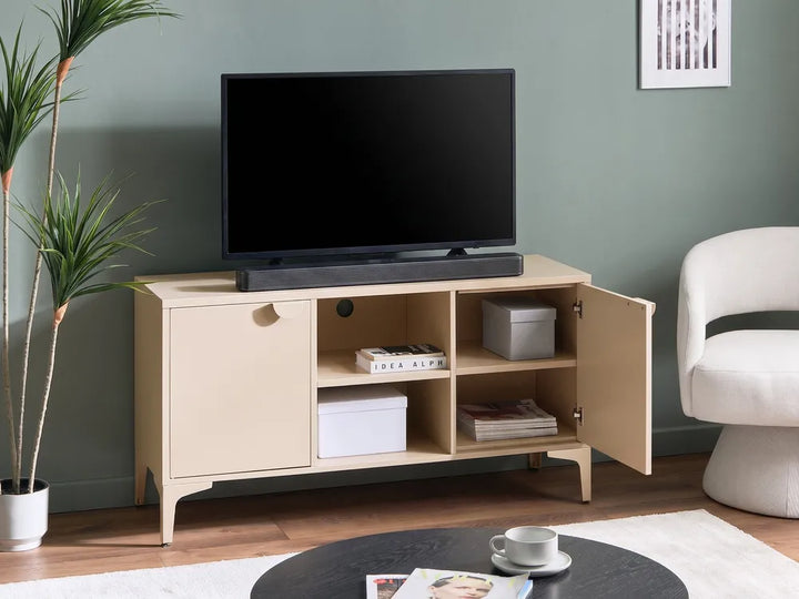 A light beige wooden TV stand cabinet with open shelves and a side door, holding a black television and storage boxes, set in a living room against a sage green wall.