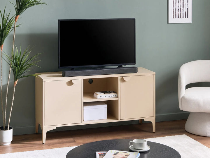 A light beige wooden TV stand cabinet with two doors and an open center shelf, holding a black flat-screen TV and a soundbar, set against a sage green wall in a styled living room.