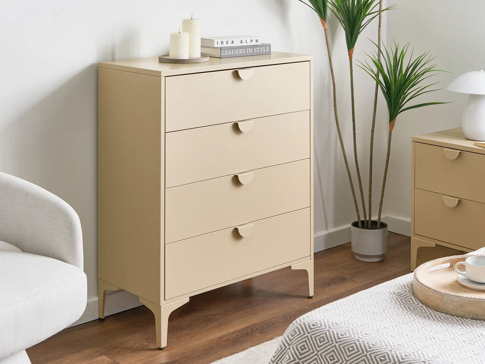 A light beige four-drawer chest of drawers with small round knobs and tapered legs, styled in a bedroom next to a bed, a nightstand, and a potted plant.